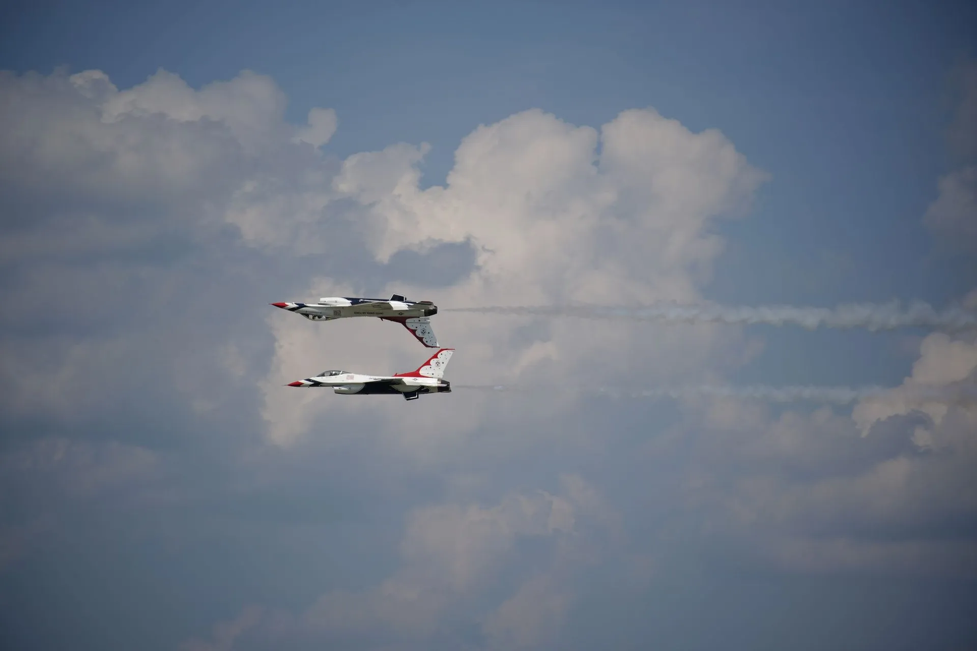 Two fighter jets perform an aerial maneuver against a cloudy sky in