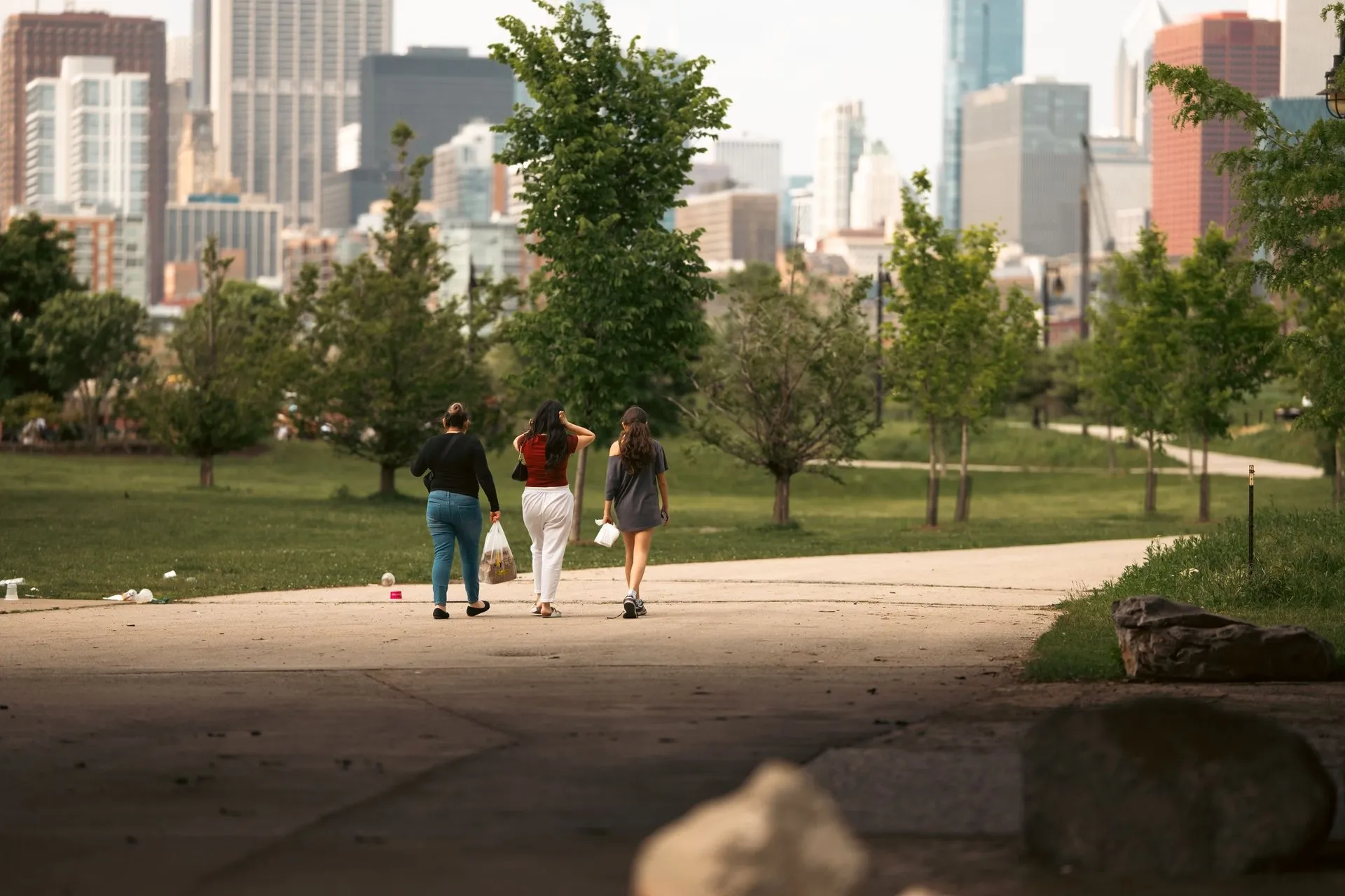 Three young women walking together through a park with Chicago skyline