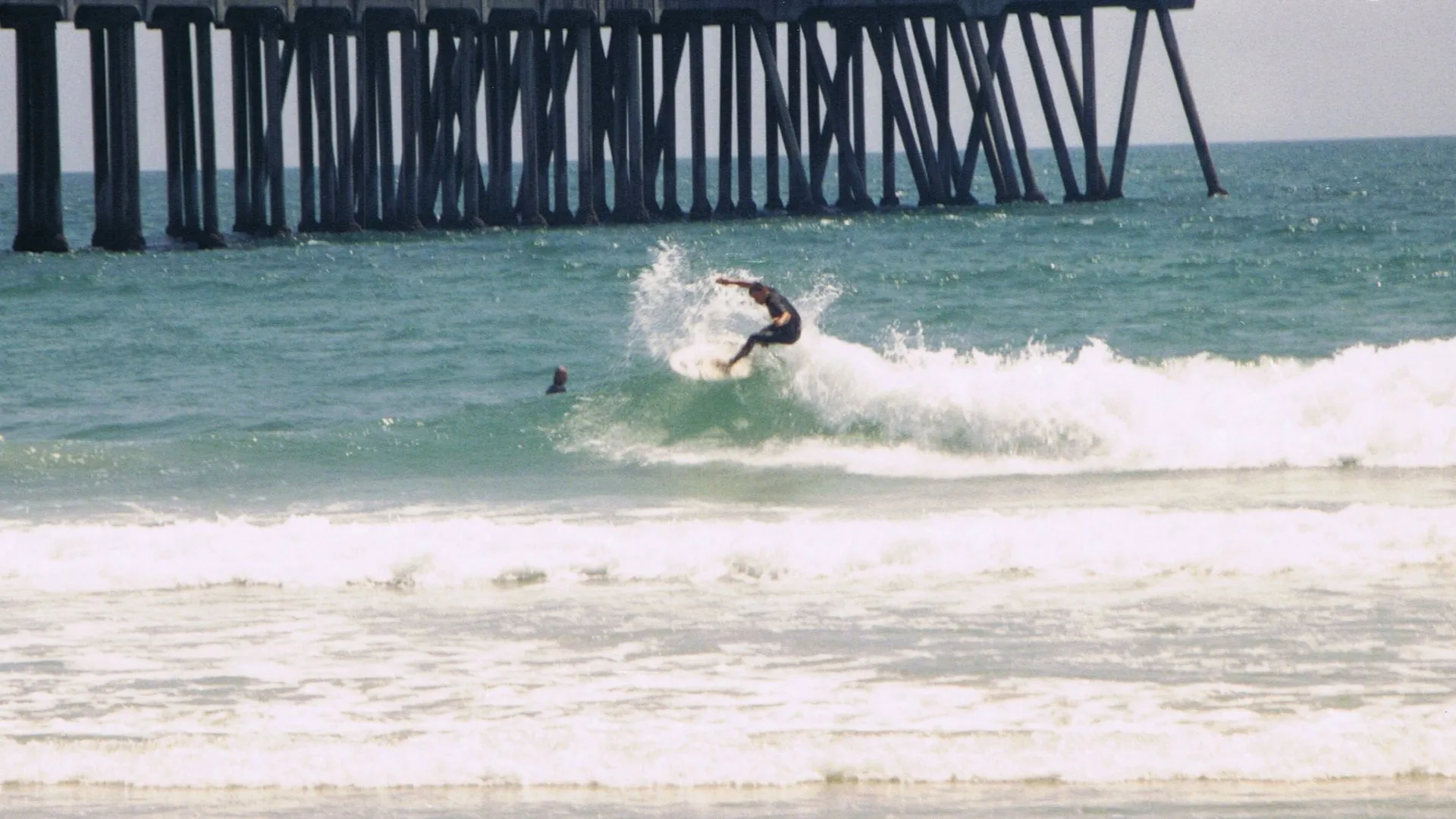 A surfer catches a wave near the iconic Huntington Beach Pier