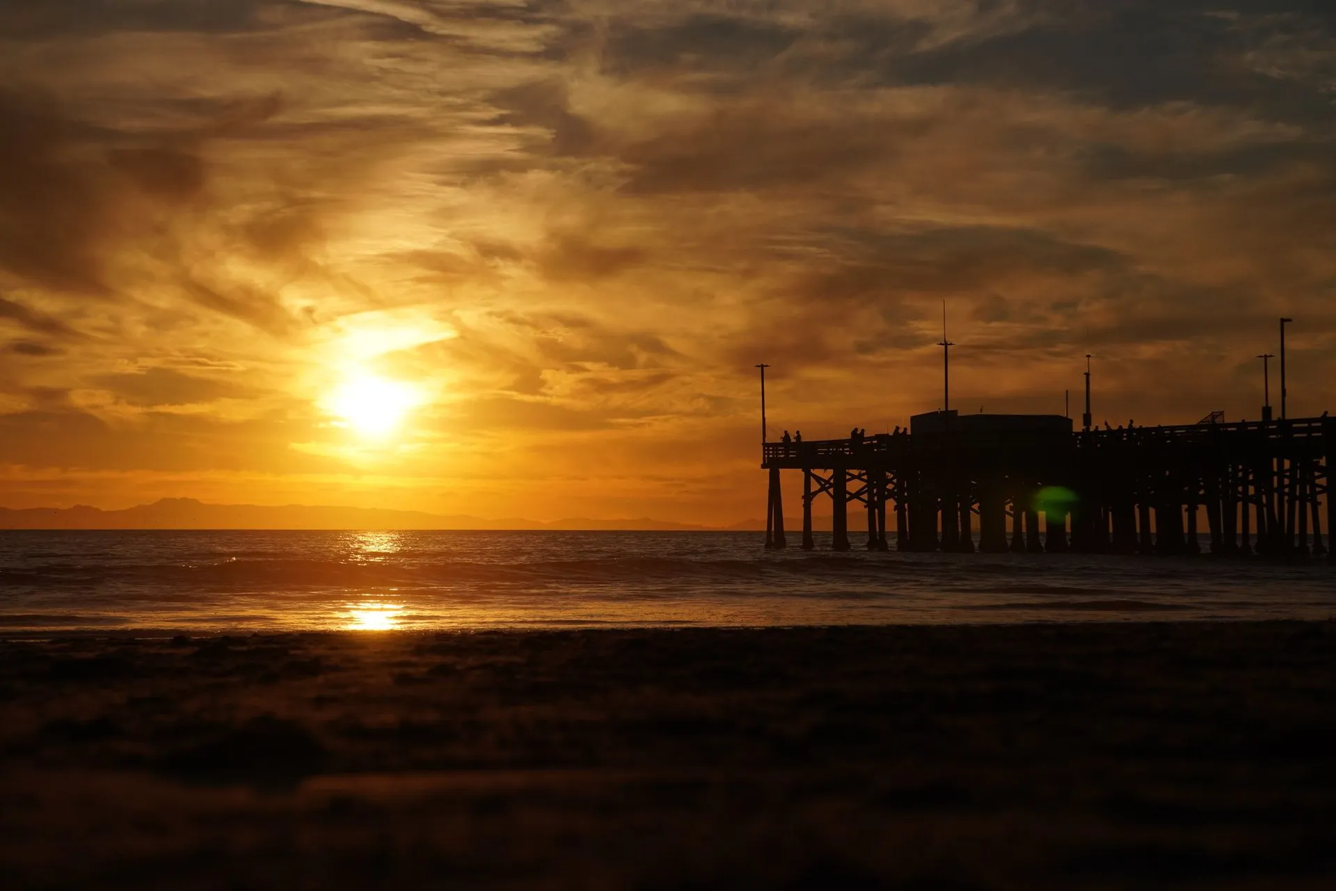 Golden sunset over Newport Beach pier with crashing waves and a vibrant sky