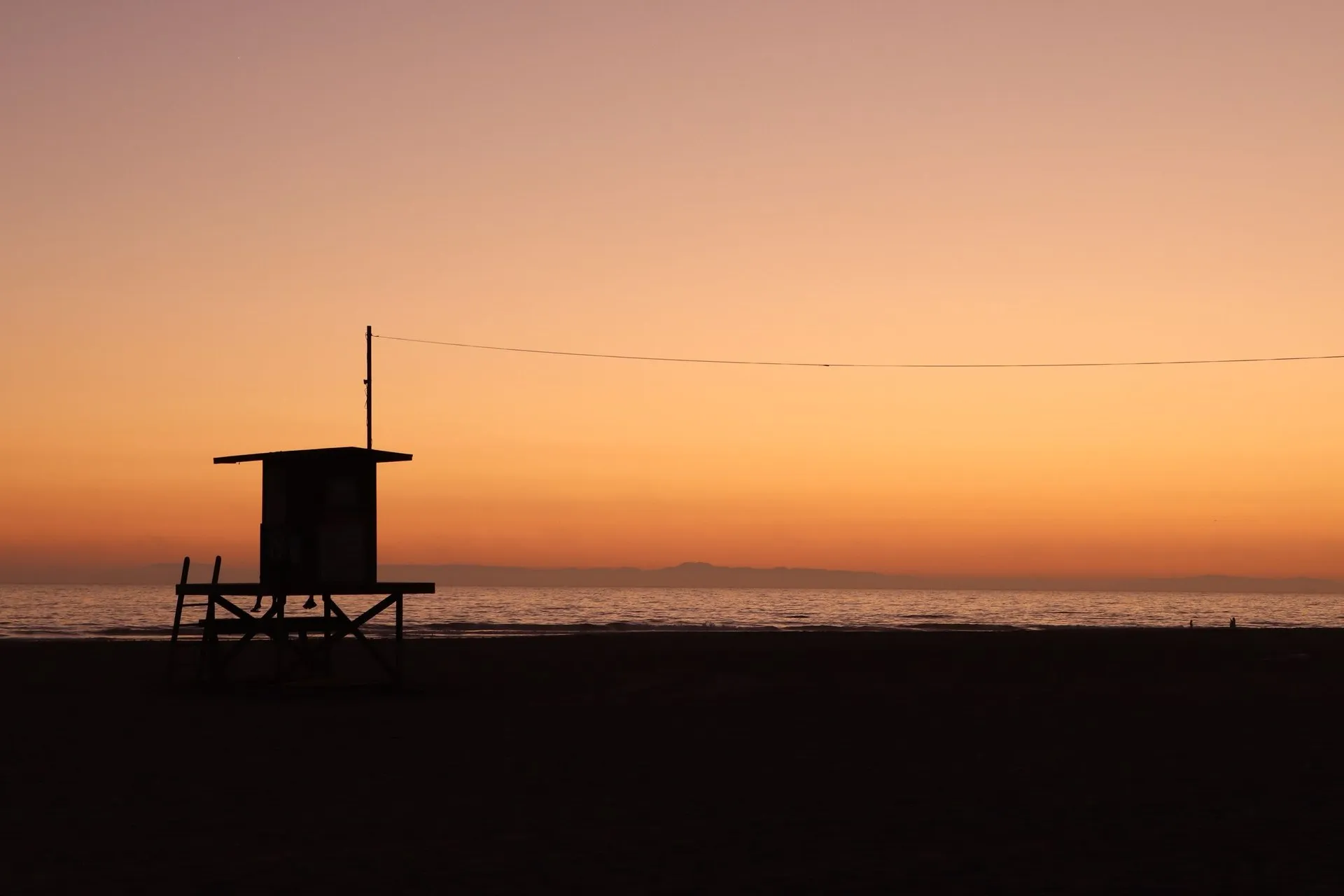 Lifeguard tower silhouette against a vivid Newport Beach sunset