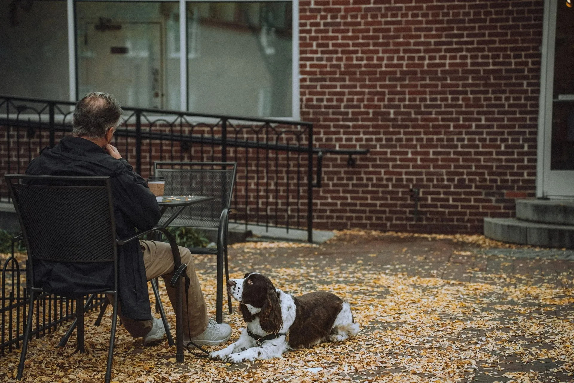 Elderly man sits with a cup of coffee while his dog relaxes