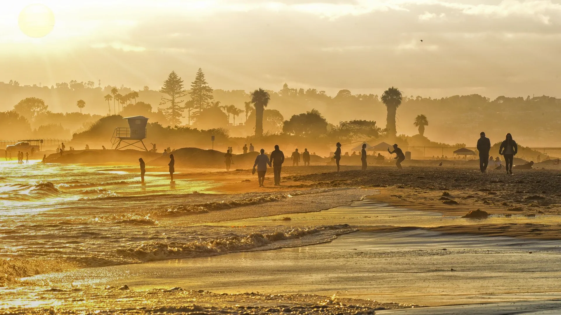 Sunset over San Diego beach with people silhouetted against golden skies